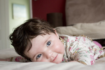 baby girl wearing white and pink top lying on bed thumbnail
