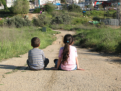 girl and boy sitting on concrete road watching village during daytime thumbnail