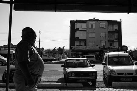 grayscale photography of man standing in front of two parked vehicles while wearing sunglasses thumbnail