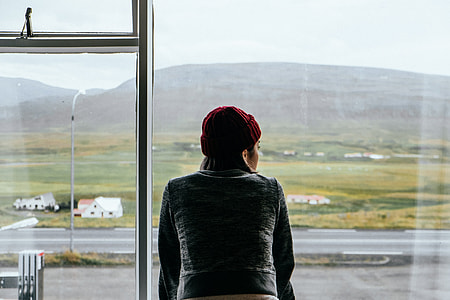 woman wearing gray coat and red knit cap looking at distance over clear glass window thumbnail