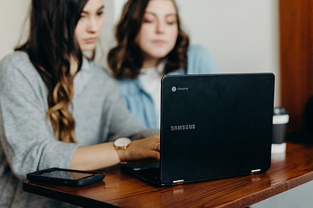 two women sitting beside black Samsung Chromebook on wooden table thumbnail