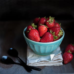 bowl of strawberries on white paper beside two black spoons thumbnail