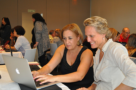 two woman using MacBook on white wooden table thumbnail