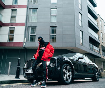 person in red jacket leaning on black Bentley Mulsane parked on road side thumbnail