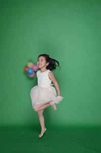girl holding balloons jumping on green surface thumbnail