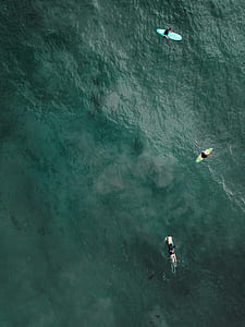 aerial photo of three persons with surfboards on body of water during daytime thumbnail
