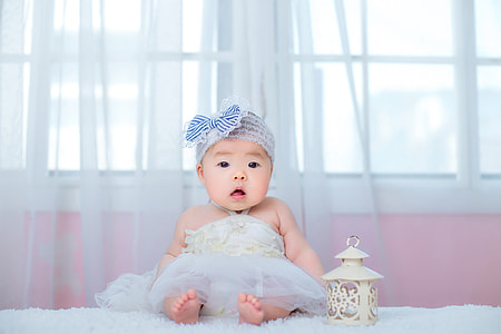 baby sitting beside candle lantern near curtain thumbnail
