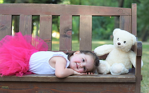 girl lying on brown bench beside bear plush toy at daytime thumbnail