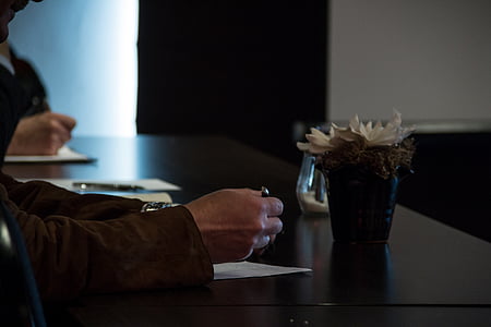 person holding pen near flower vase on black surface thumbnail