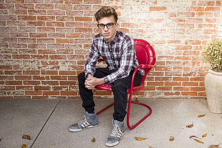 Man In Plaid Long-Sleeved Shirt And Black Pants Sitting On Red Chair thumbnail
