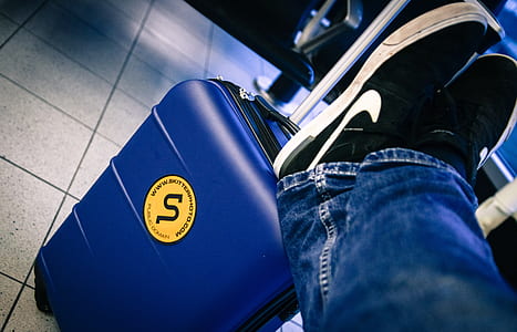 person wearing blue jeans resting foot on blue luggage thumbnail