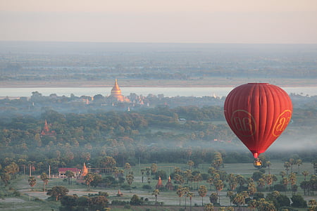 red hot air balloon flying over trees thumbnail