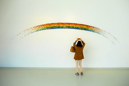 Woman Wearing Brown Top and Beige Leggings Taking Picture Rainbow Painted Wall thumbnail