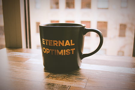 focus photography of black Eternal Optimist graphic ceramic mug on table near window thumbnail
