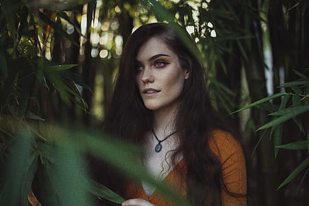 woman wearing orange shirt standing near green plant thumbnail