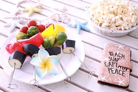 vegetable skewers on round ceramic plate near popcorn and brown leather flip phone case on white wooden surface thumbnail