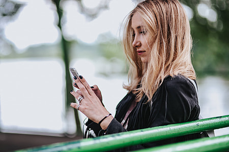 Blonde woman in a black jacket and ripped jeans by a green handrail thumbnail