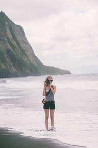 woman holding black instant camera standing on beach during daytime thumbnail