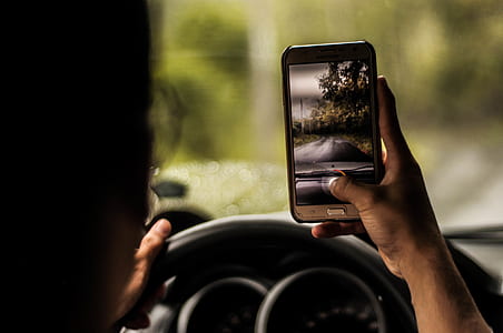 person holding gold smartphone near vehicle steering wheel thumbnail