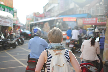 woman facing back with beige backpack standing beside motorcycle thumbnail