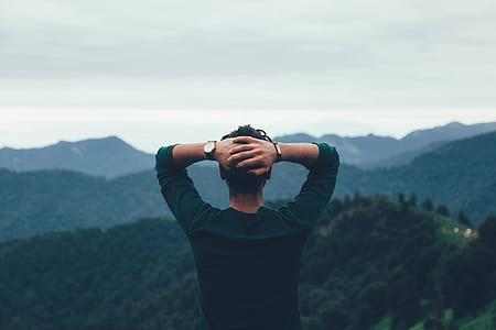 man with arms behind his head facing the forest during day thumbnail