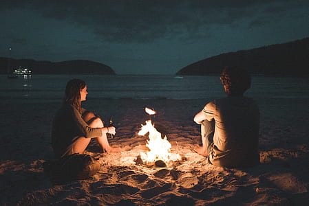 bonfire between man and woman near sea during nighttime thumbnail