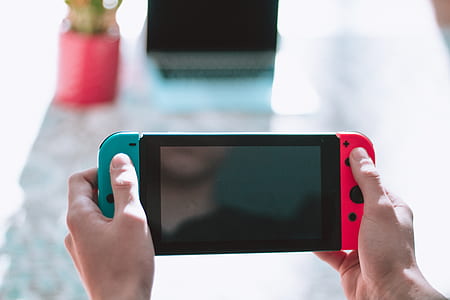 person holding Nintendo Switch in front of glass table during daytime shallow focus photography thumbnail