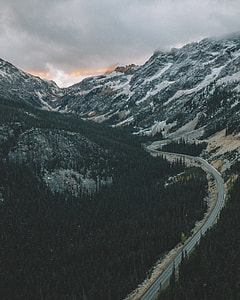 road between trees background of mountain under cloudy sky thumbnail