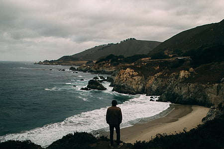 person standing on cliff near seashore during daytime thumbnail