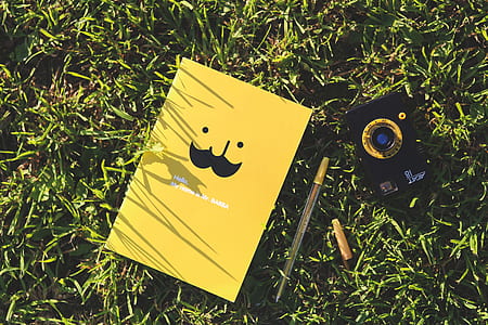 yellow book beside ballpen on green grass thumbnail