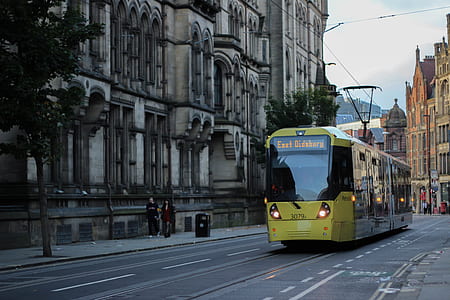 yellow and black train on road near concrete building during daytime thumbnail
