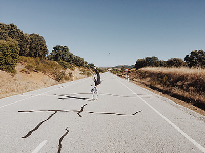 person performing stunts in middle of road near trees during daytime thumbnail