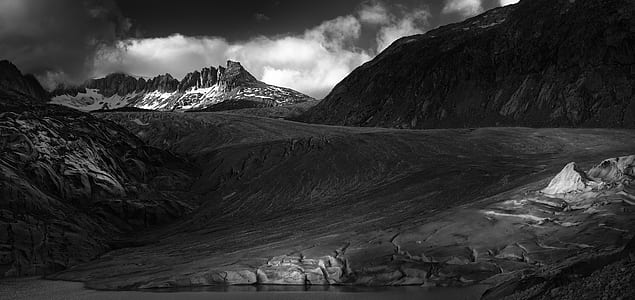 grayscale photography of rocky mountain under white clouds thumbnail