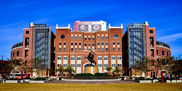 photo of brown and gray concrete building near person riding horse statue under clear blue sky thumbnail