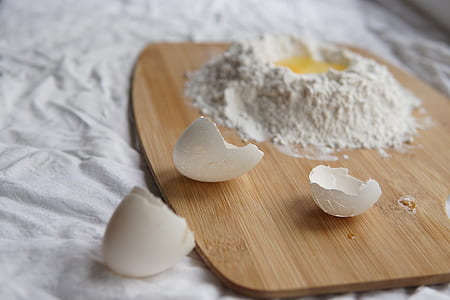 egg shell on brown chopping board beside flour with egg inside thumbnail