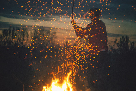 man holding a stick in front of a firewood thumbnail