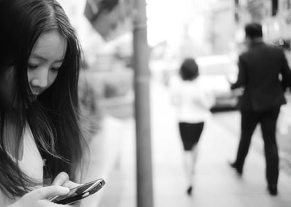 Woman Using Smartphone at Sidewalk Near Man and Woman Walking Away from Her thumbnail