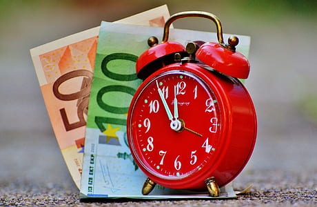 selective focus photography of red alarm clock on top of banknotes thumbnail