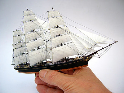 person holding white and black miniature galleon ship thumbnail