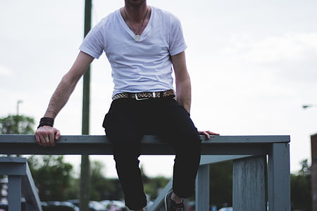 man in white shirt and black pants sitting on gray fence thumbnail