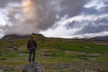 standing man wearing black hoodie on stone under gray sky thumbnail
