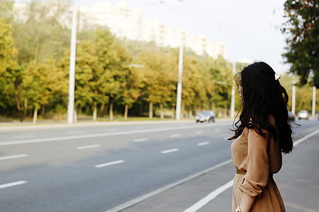 woman in brown long-sleeved dress standing in front of asphalt road during daytime thumbnail