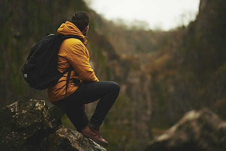 man with yellow hoodie sitting on rock boulder thumbnail
