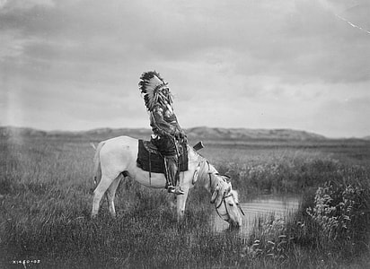grayscale photography of Native American ride-on horse in grass field thumbnail