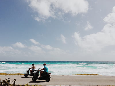 two person riding motor scooters on road near ocean during daytime thumbnail