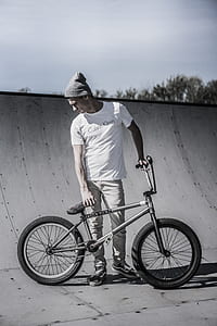 grayscale photo of man standing while holding bike thumbnail