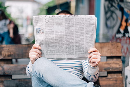 person holding newspaper while sitting on bench thumbnail