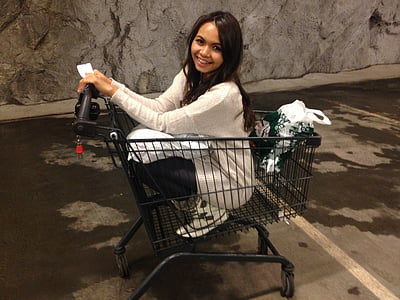 smiling woman riding black shopping cart near gray wall thumbnail