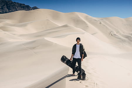 man wearing black jacket and white shirt holding white board over sandy ground thumbnail