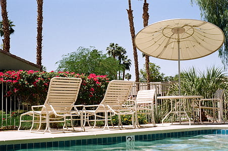 two white lounge chairs besides patio table and umbrella and pool thumbnail